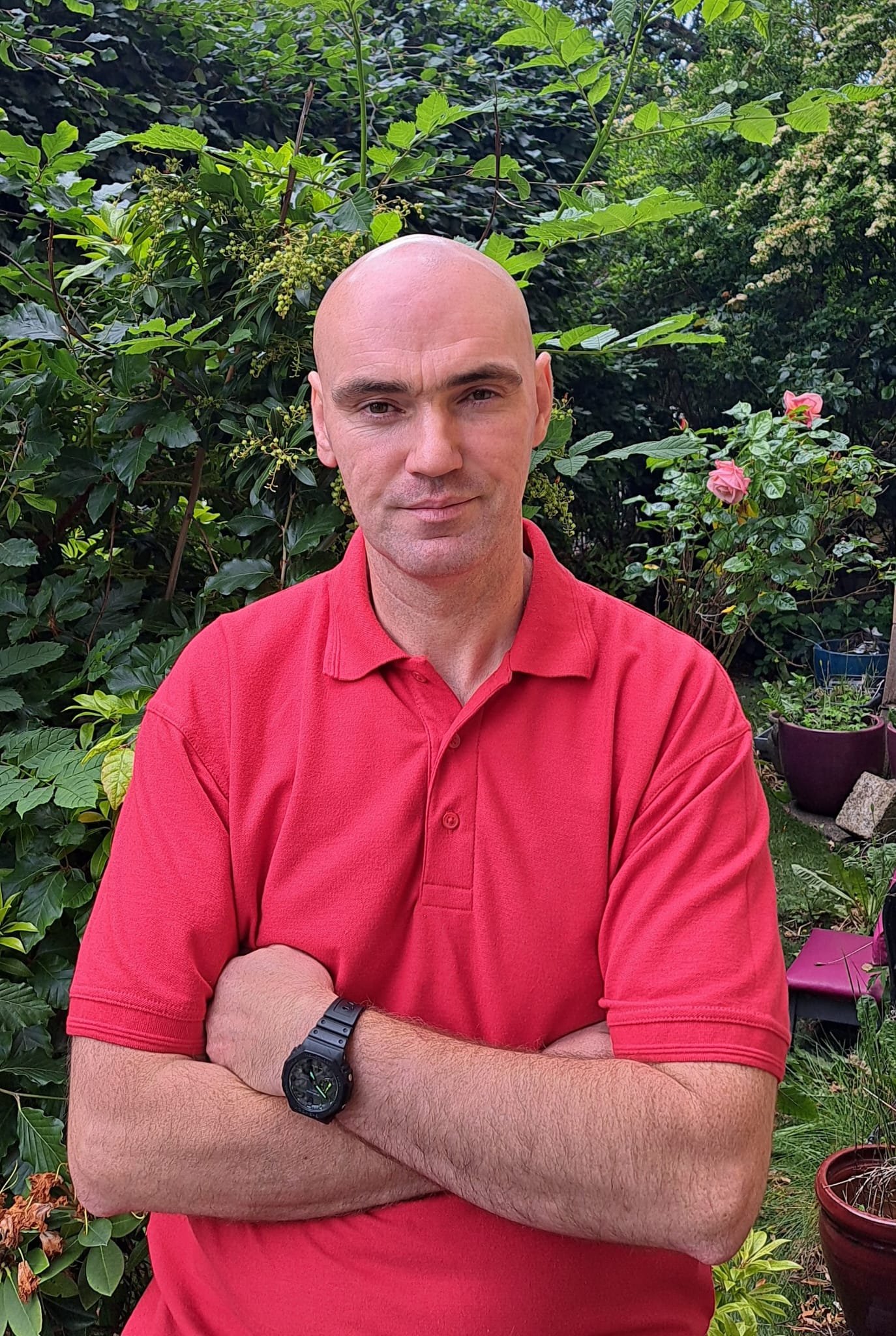 Kevin Black, owner of Glasgow West End Van Man, standing in a garden wearing a red polo shirt with arms crossed